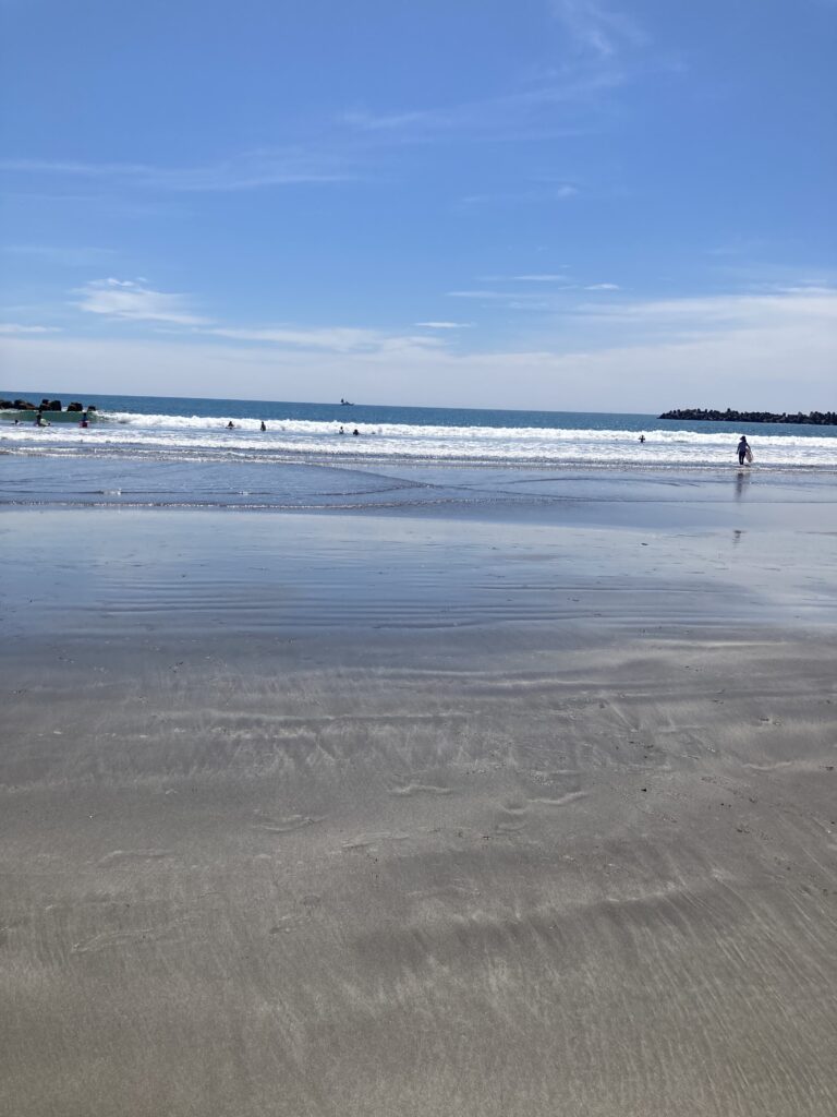 前原海水浴場の砂浜。浅瀬で海水浴を楽しんでいる人がいる。